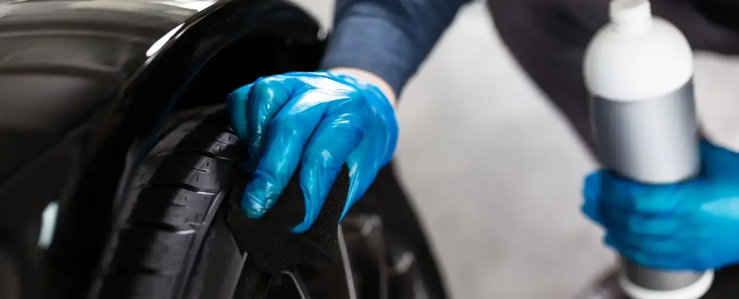 Detailer applying tire dressing to a black tire with a foam applicator pad.
