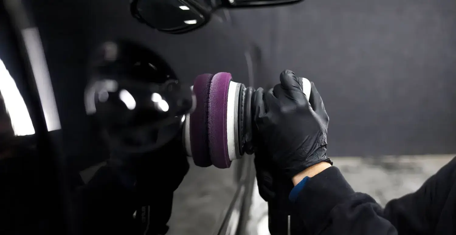 Professional detailer polishing a black car door with a dual action polisher and foam pad