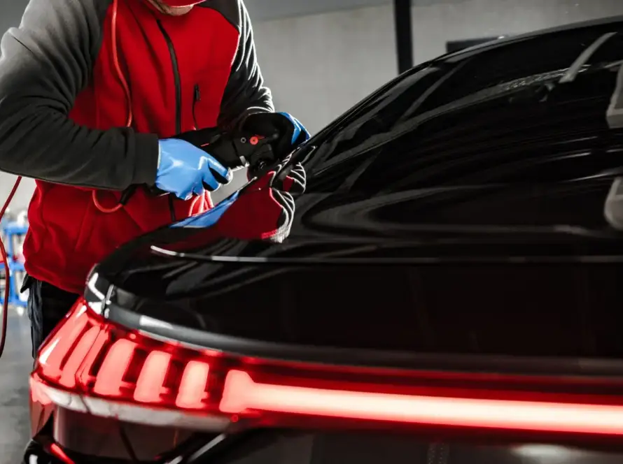 Professional car detailer polishing black vehicle under bright lights