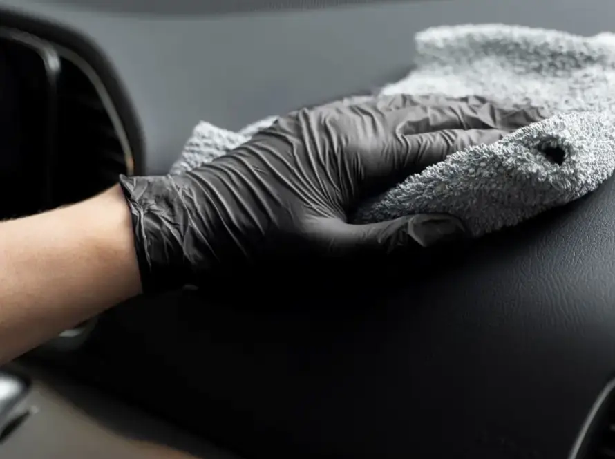 Detailer wiping black dashboard with gray microfiber cloth wearing gloves