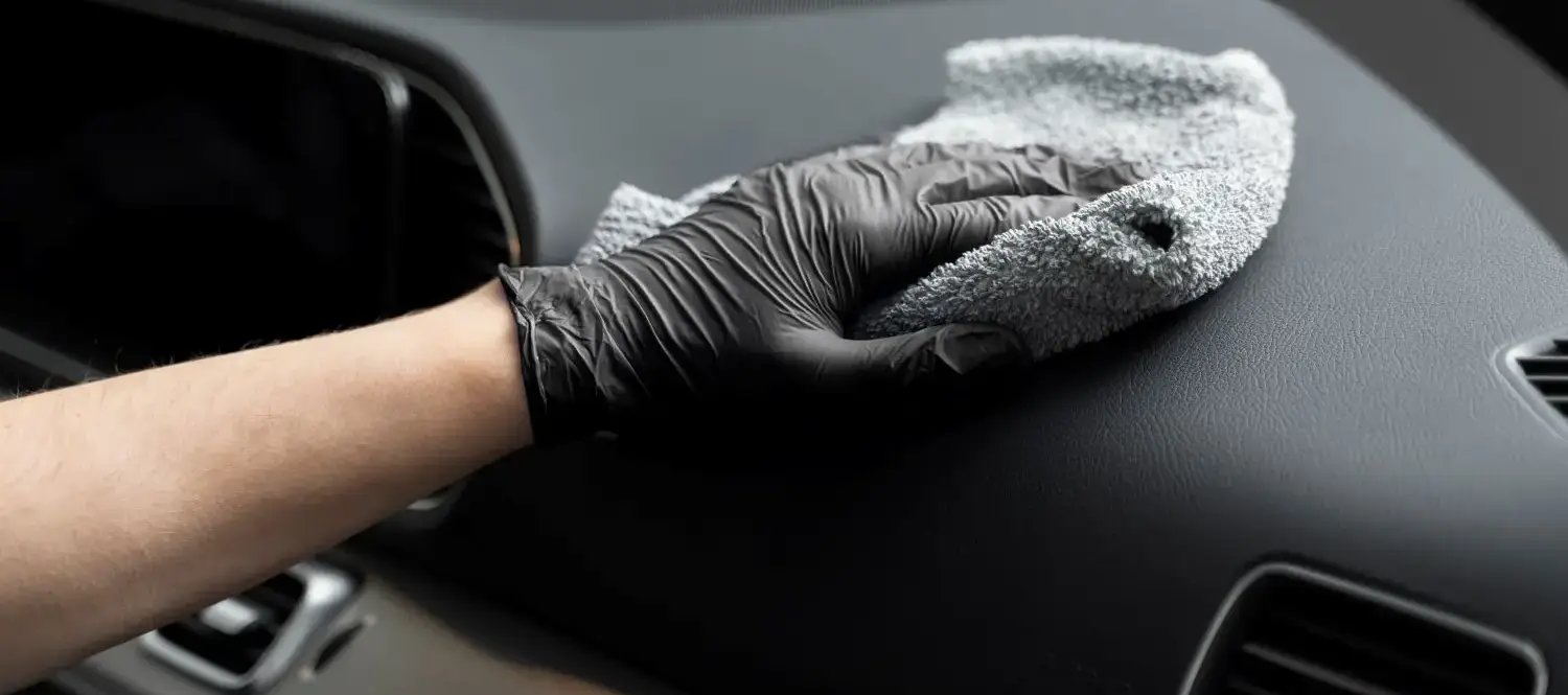 Detailer wiping black dashboard with gray microfiber cloth wearing gloves