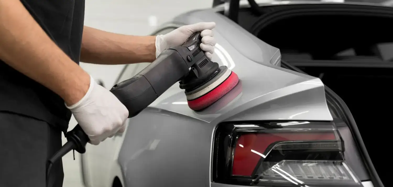 Detailer using a dual action polisher with red pad on a silver car rear quarter panel.