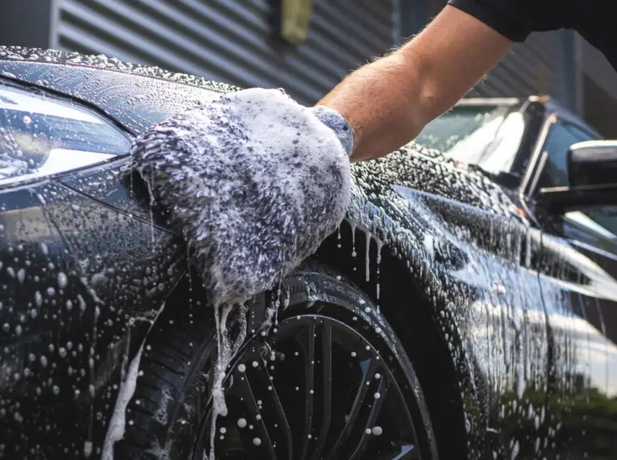 Grey wash mitt gliding over soapy black car fender